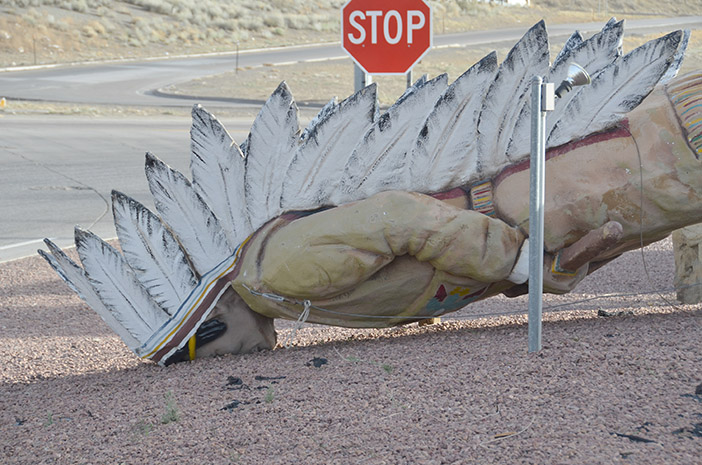 Statue of Indian Chief lying face down in gravel next to a STOP sign